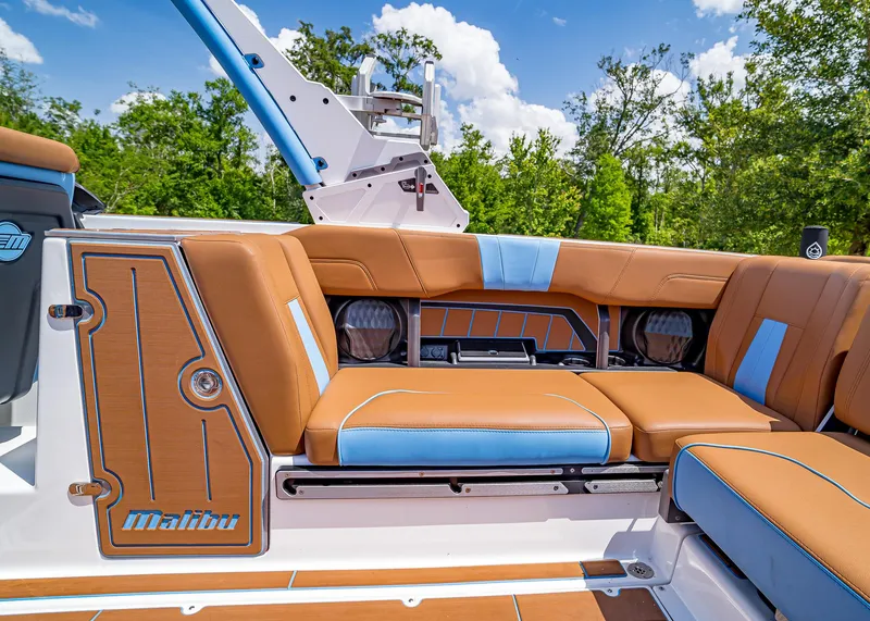 Slide: The Image of 2024 Malibu Wakesetter 24 MXZ interior with tan and blue seating, surrounded by lush greenery. - 28