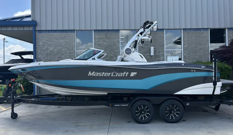 Slide: The Image of 2018 MasterCraft XT23 boat on trailer, parked outside a building. - 0