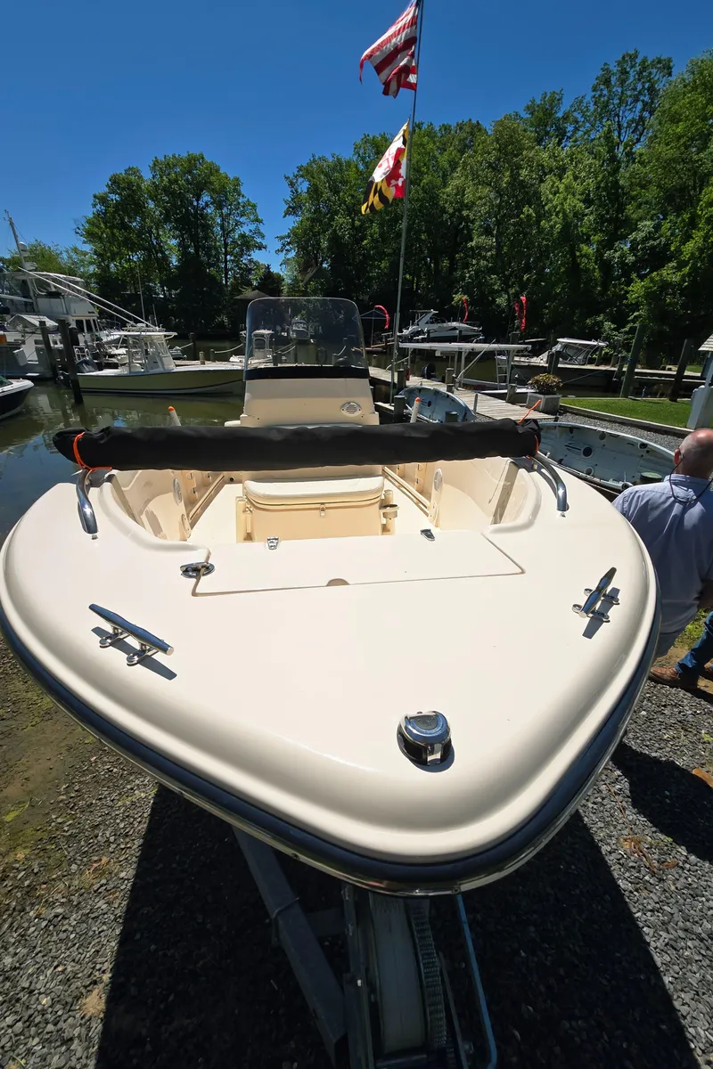 Slide: The Image of 2023 Grady-White Fisherman 180 boat on trailer, dockside with flags and trees in background. - 25