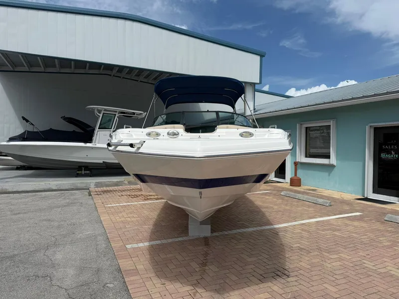 Slide: The Image of 2018 NauticStar 243DC Sport Deck boat parked outside, featuring a sleek design and blue canopy. - 3