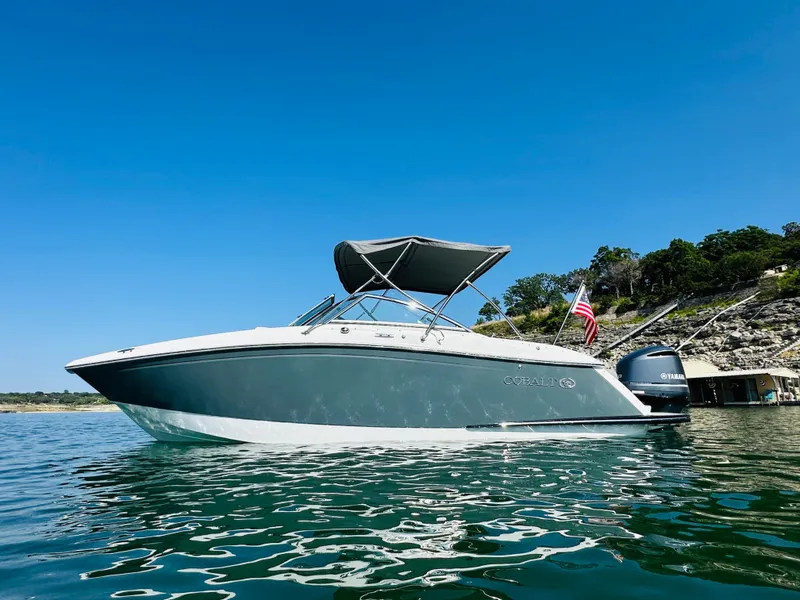 Slide: The Image of 2018 Cobalt 23SC boat on water, clear sky, American flag, scenic background. - 1