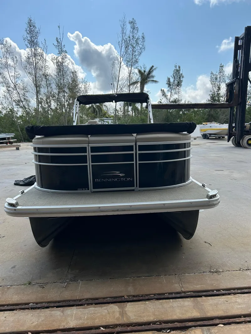 Slide: The Image of 2014 Bennington 2550 RCB pontoon boat on a dock, surrounded by trees and blue sky. - 2
