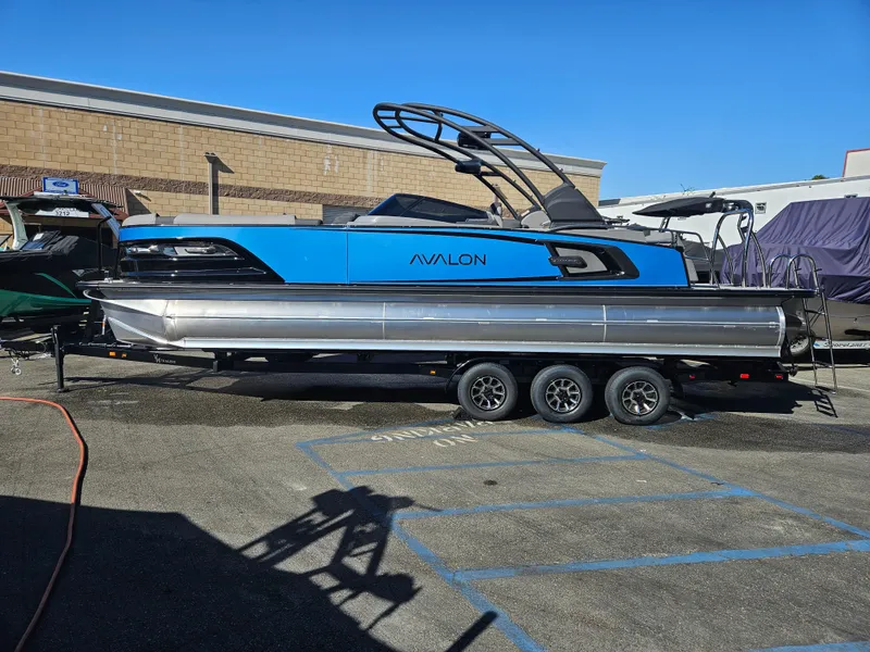 Slide: The Image of 2025 Avalon Excalibur LTD Elite Windshield 27FT pontoon boat on trailer, blue and silver design. - 10