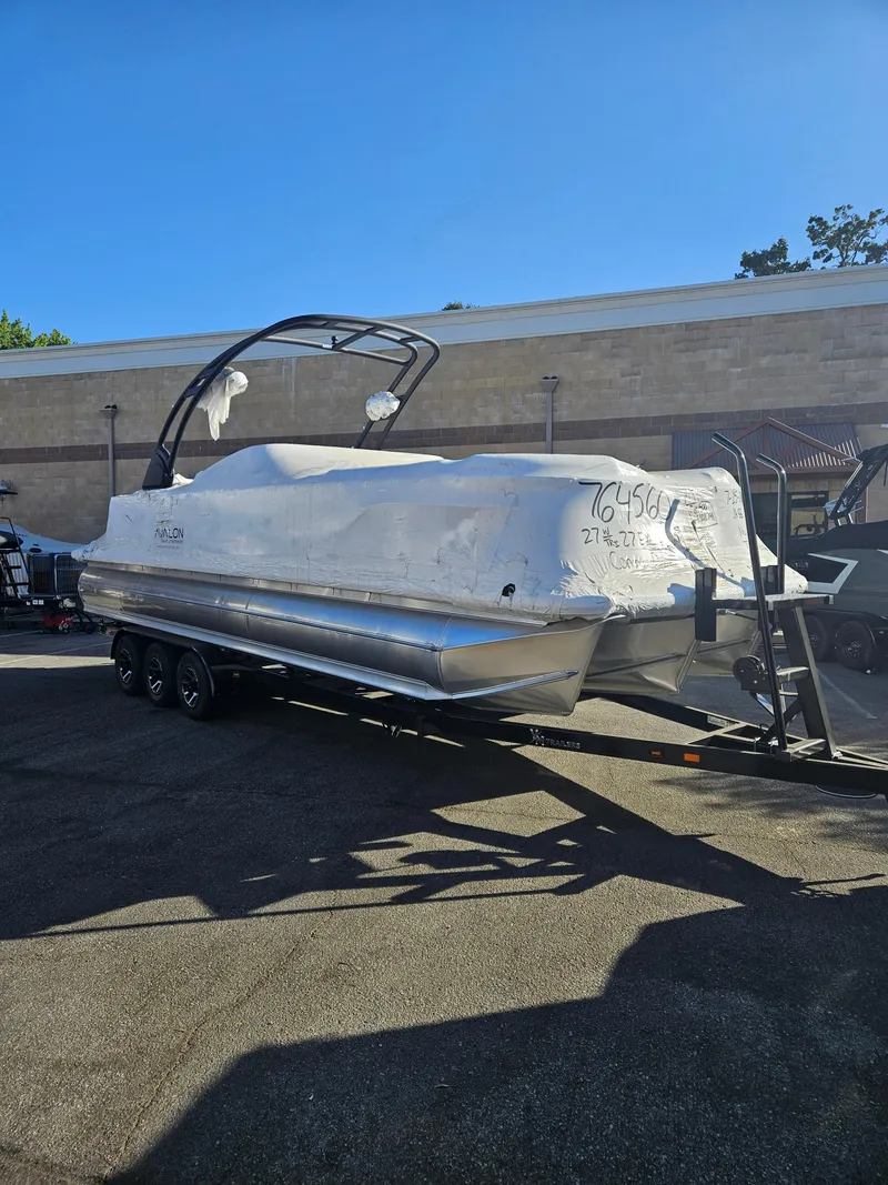 Slide: The Image of 2025 Avalon Excalibur LTD Elite Windshield 27FT boat on trailer, covered and parked outdoors. - 12