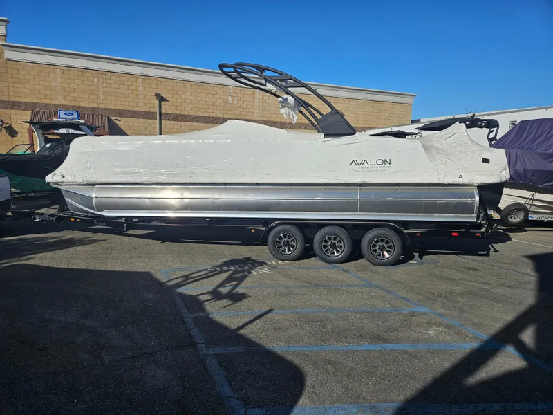Slide: The Image of 2025 Avalon Excalibur LTD Elite Windshield 27FT boat covered, parked on a trailer. - 13