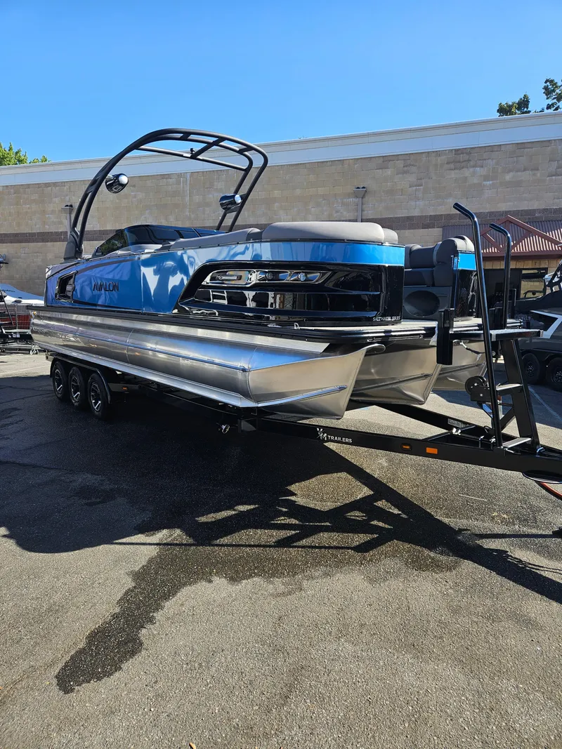 Slide: The Image of 2025 Avalon Excalibur LTD Elite Windshield 27FT pontoon boat on trailer, parked outdoors. - 8