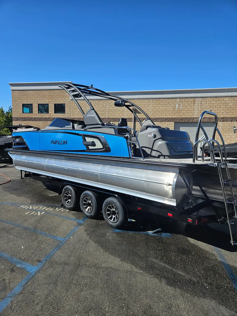 Slide: The Image of 2025 Avalon Excalibur LTD Elite Windshield 27FT boat on trailer, parked outdoors. - 9