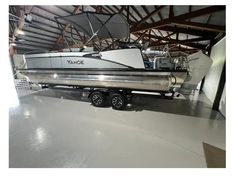 Slide: The Image of 2025 Tahoe CASCADE pontoon boat in a warehouse, featuring a sleek design and modern outboard motor. - 1