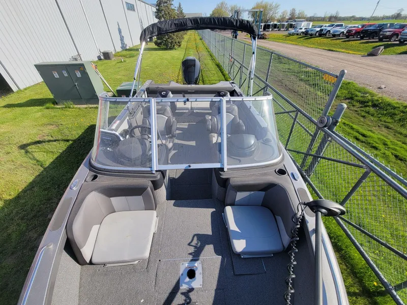 Slide: The Image of 2018 Crestliner 1950 Sportfish SST boat with seating, windshield, and canopy, parked near a fence. - 15
