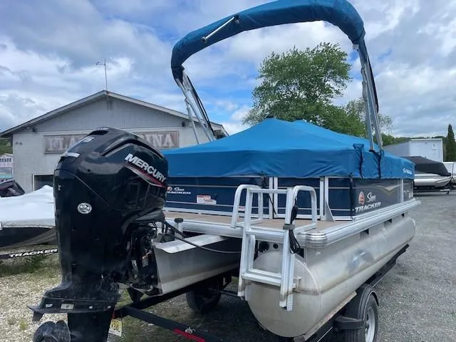 Slide: The Image of 2020 Sun Tracker Party Barge 18 DLX with Mercury engine, covered and parked outdoors. - 2