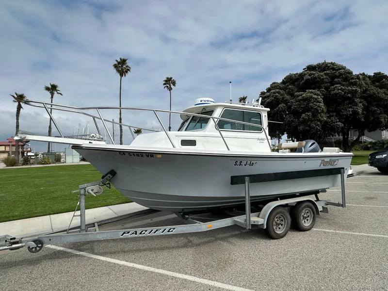 Slide: The Image of 2019 Parker 2120 Sport Cabin boat on trailer, parked near palm trees and greenery. - 0