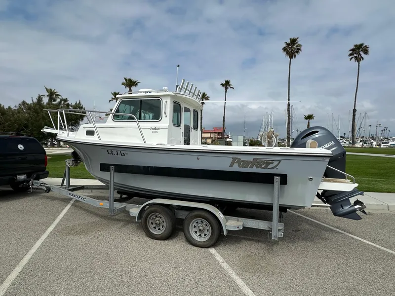 Slide: The Image of 2019 Parker 2120 Sport Cabin boat on trailer in parking lot with palm trees. - 1