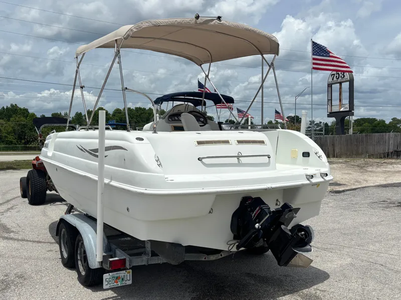 Slide: The Image of 2002 Monark Sunlounger 215 boat on trailer, parked outdoors with American flags in background. - 2