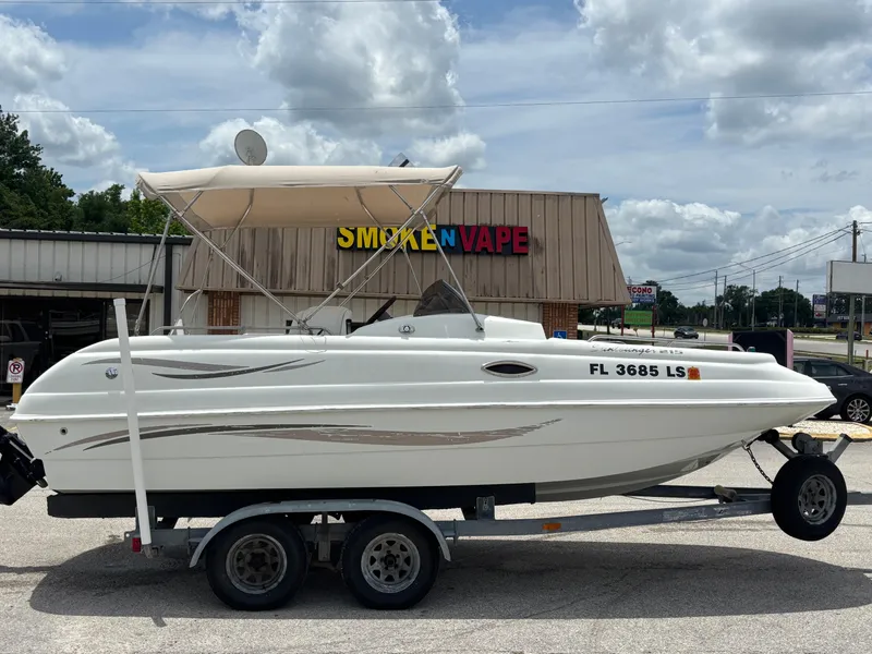 Slide: The Image of 2002 Monark Sunlounger 215 boat on trailer, parked near a vape shop. - 5