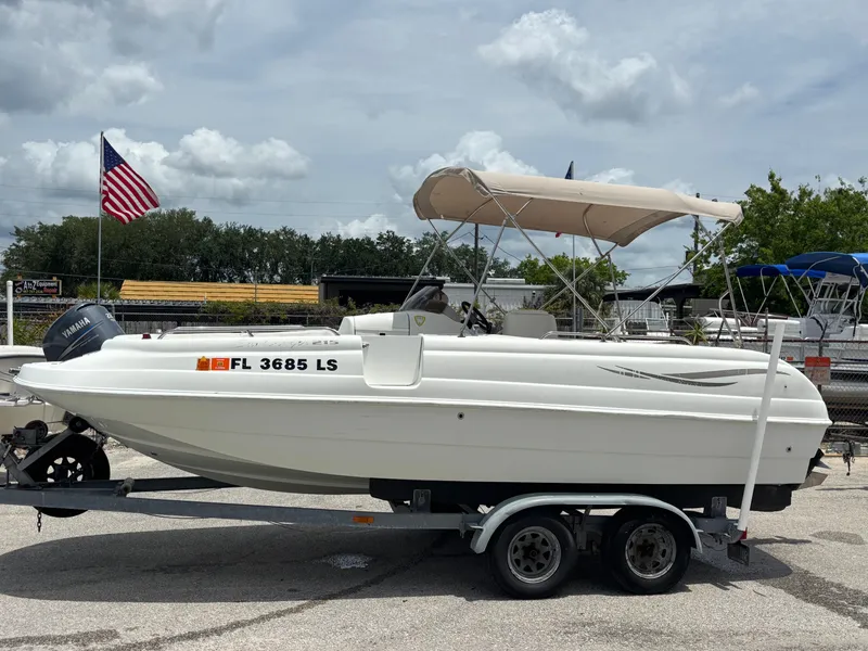 Slide: The Image of 2002 Monark Sunlounger 215 boat on trailer, parked outdoors, with American flag in background. - 9