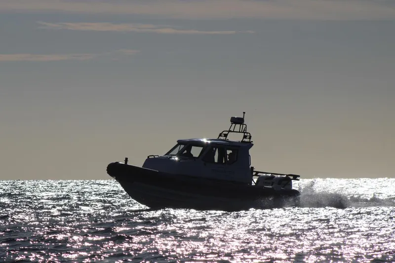 Slide: The Image of Silhouetted Fluid Watercraft Patrol 880 Cabin cruising on shimmering water at sunset, 2022 model. - 3
