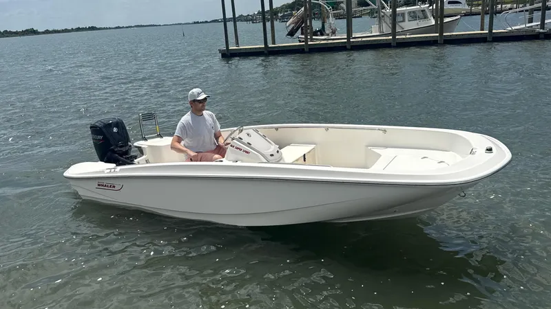 Slide: The Image of 2023 Boston Whaler 160 Super Sport boat on water with driver, near dock. - 14