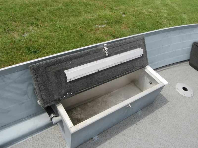 Slide: The Image of Open storage compartment on 2018 Starcraft SF DLX 16 boat, with gray interior and grassy background. - 18
