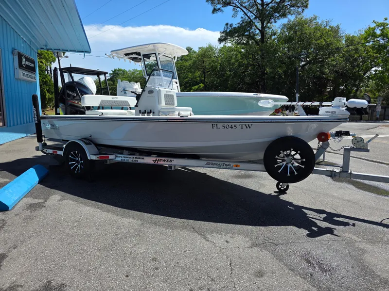 Slide: The Image of 2024 Hewes Redfisher 18 boat on trailer, parked outdoors near a blue building. - 1