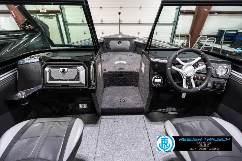 Slide: The Image of 2025 Lund 1875 Tyee boat interior with steering wheel and seating, showcased in a showroom. - 17