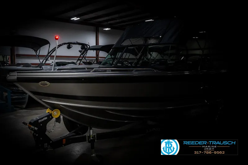 Slide: The Image of 2025 Lund 1875 Tyee boat in showroom, side view with trailer, dim lighting. - 4
