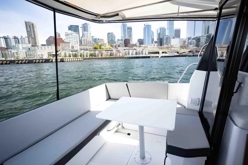 Slide: The Image of 2022 Jeanneau NC Weekender 895 boat with city skyline view, featuring a cozy seating area. - 7