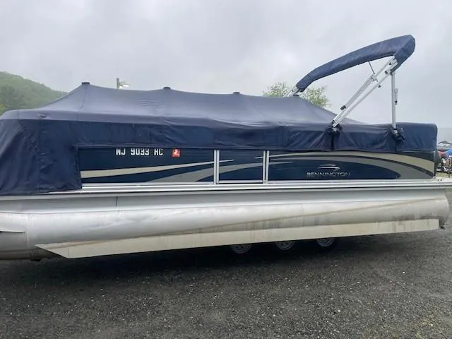 Slide: The Image of 2011 Bennington 2275GLi pontoon boat with blue cover, parked on gravel. - 0