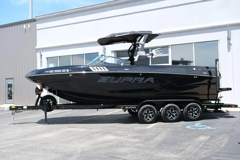 Slide: The Image of 2019 Supra SE450 boat on trailer, sleek black design, parked outside a building. - 2