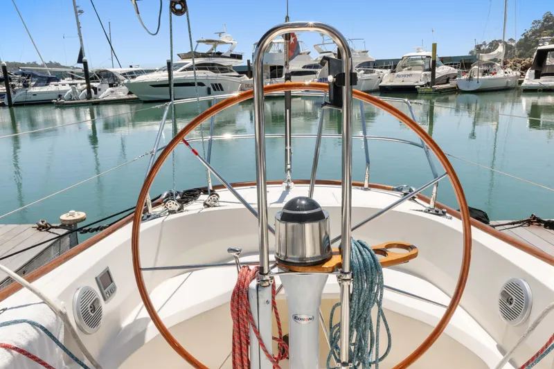 Slide: The Image of 2008 Sabre Spirit sailboat helm with marina view, featuring wooden wheel and nautical ropes. - 28