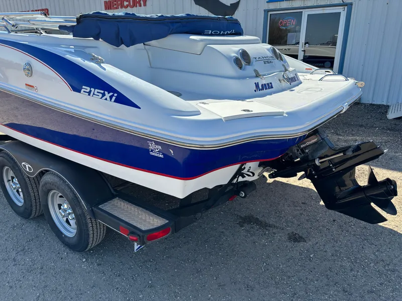 Slide: The Image of 2020 Tahoe 215 Xi boat on trailer, featuring blue and white design, parked outside a building. - 3