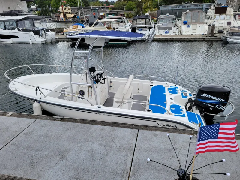 Slide: The Image of 2005 Boston Whaler 180 Dauntless boat docked, featuring a Mercury 135 engine and blue seating. - 2