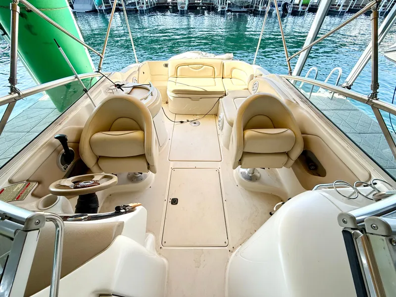 Slide: The Image of 2002 Sea Ray 270 Sundeck interior with beige seating and steering wheel, docked by the water. - 3