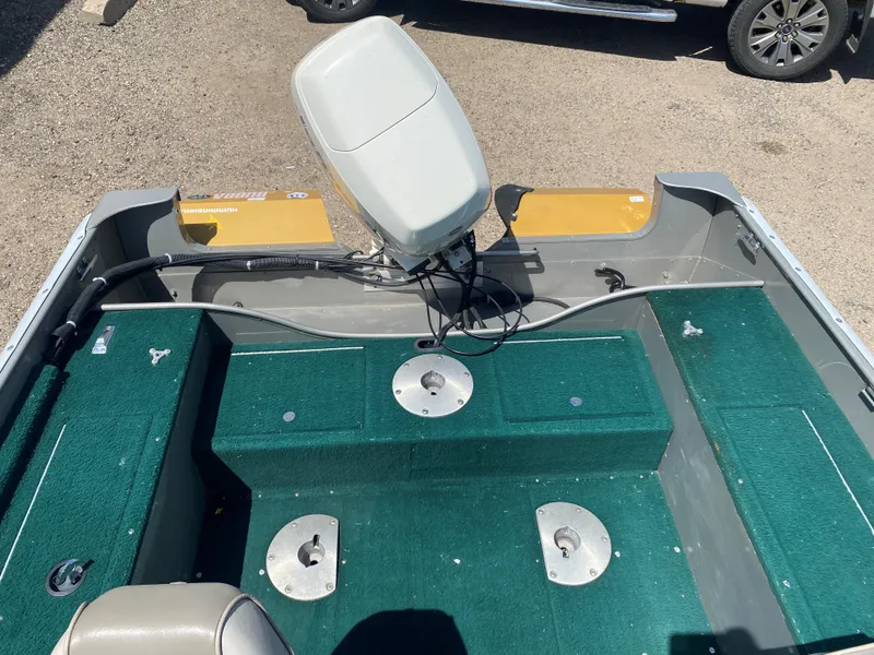 Slide: The Image of 2002 Lund 1650 Explorer boat interior with green carpet and motor, parked on gravel. - 26