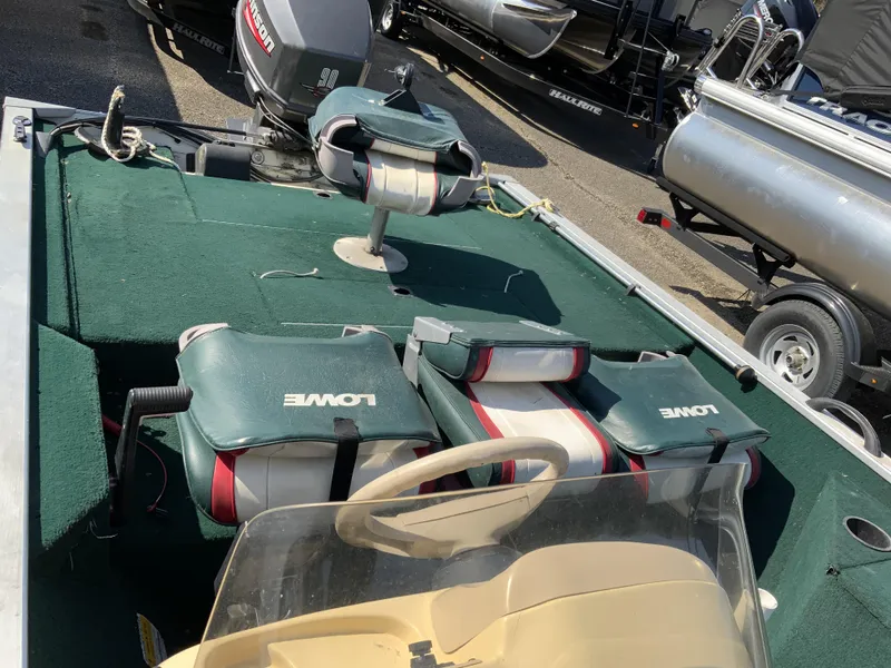 Slide: The Image of 1999 Lowe 180 boat interior with green seats and steering wheel, parked near other boats. - 11