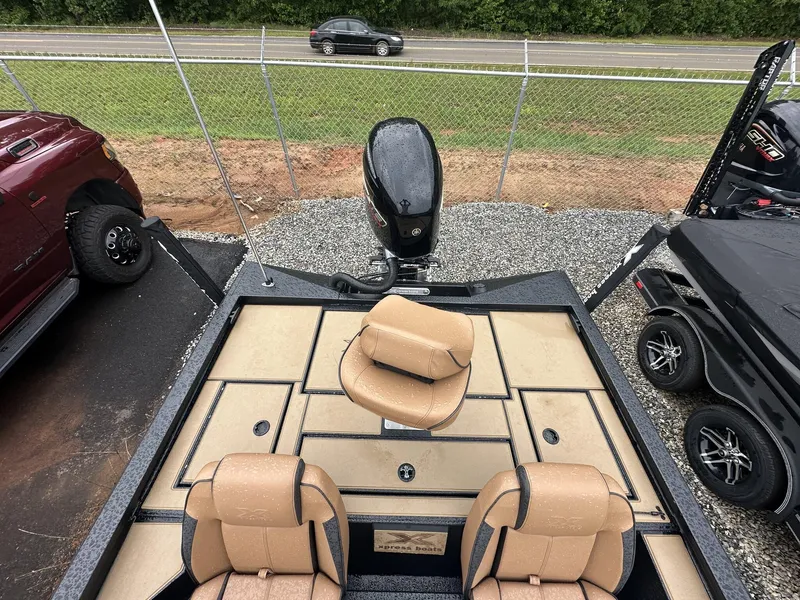 Slide: The Image of 2025 Xpress Hyper-Lift Bass Series boat with tan seats and motor, parked near a road. - 5