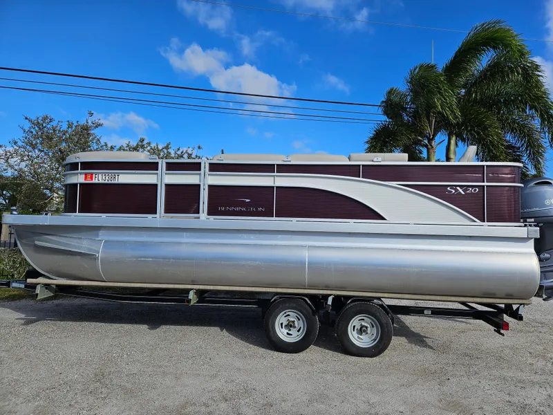 The Image of 2019 Bennington 20 SX pontoon boat on trailer, parked outdoors under blue sky. - 0