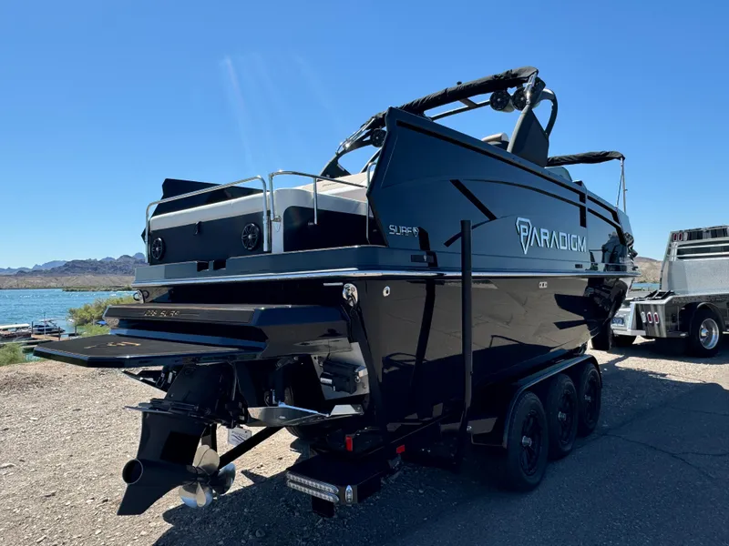 Slide: The Image of 2025 Paradigm 236 Surf SL boat on trailer by a lake, under clear blue sky. - 4