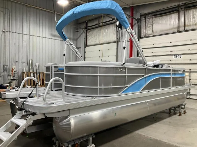 Slide: The Image of 2025 Bennington 22 SSRX pontoon boat with blue canopy in a warehouse setting. - 3