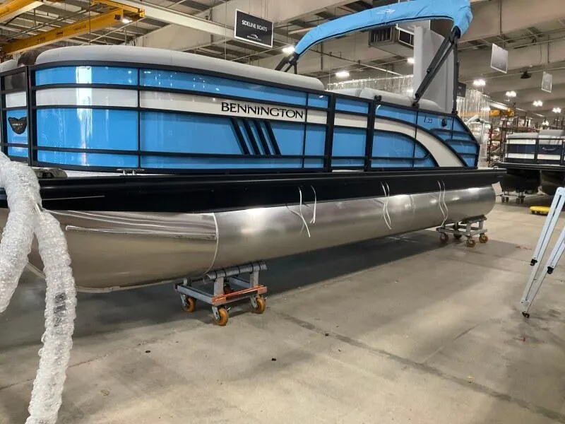 Slide: The Image of 2025 Bennington 22 LSB pontoon boat in a showroom, featuring a sleek blue and silver design. - 1
