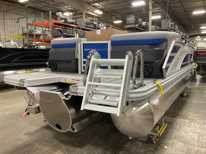Slide: The Image of 2025 Bennington 22 MFB pontoon boat in a warehouse setting, rear view with ladder. - 2