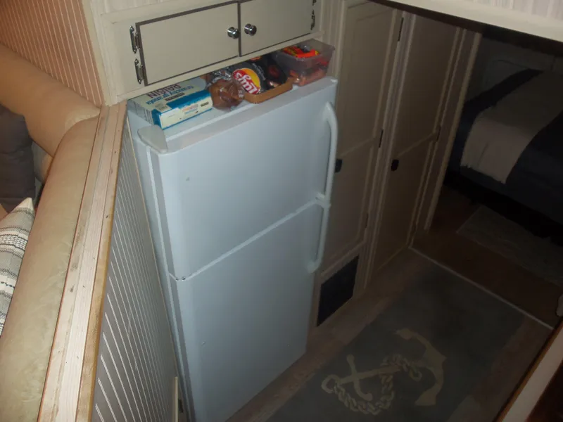 Slide: The Image of Compact kitchen area with a white refrigerator, snacks on top, and nautical-themed rug. - 34