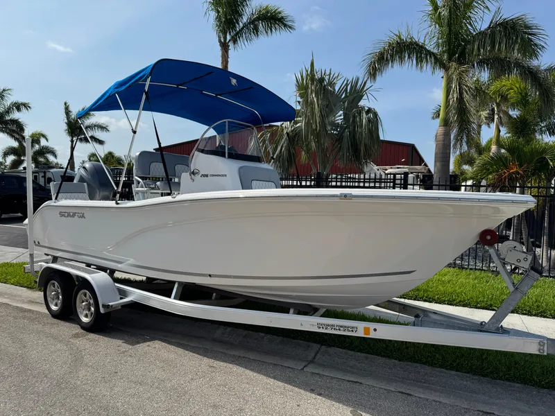 The Image of 2019 Sea Fox 206 Commander boat on trailer, blue canopy, palm trees in background. - 1
