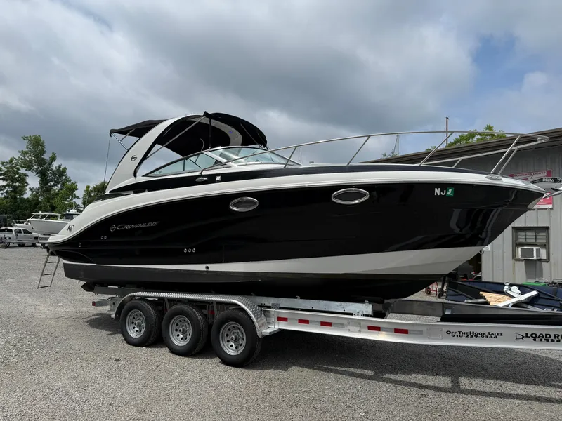 Slide: The Image of 2023 Crownline 264 CR boat on trailer, black hull, parked outdoors. - 2
