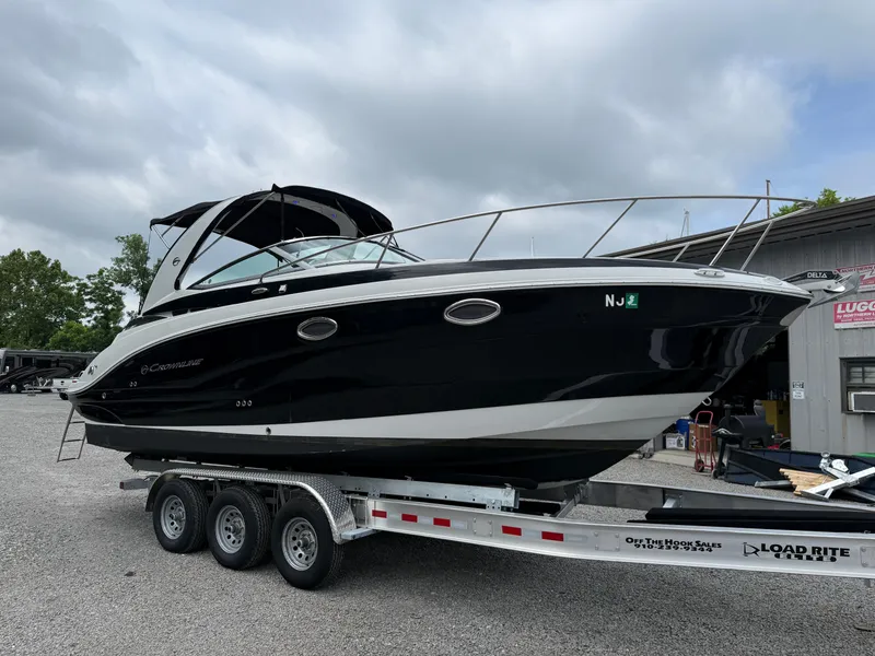 Slide: The Image of 2023 Crownline 264 CR boat on a trailer, black hull, parked outdoors. - 6
