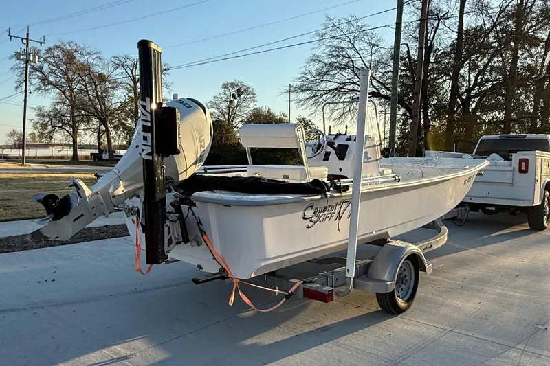 Slide: The Image of 2023 Coastal Skiff 171 boat on trailer, parked outdoors near trees and a truck. - 6