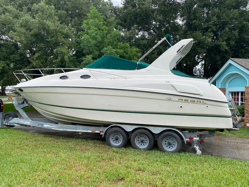 Slide: The Image of 1998 Regal 292 Commodore boat on trailer, parked on grass with trees in background. - 2