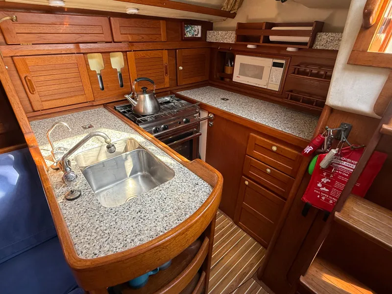 Slide: The Image of 1997 Westerly Oceanlord yacht kitchen with wooden cabinets, stove, sink, and microwave. - 33