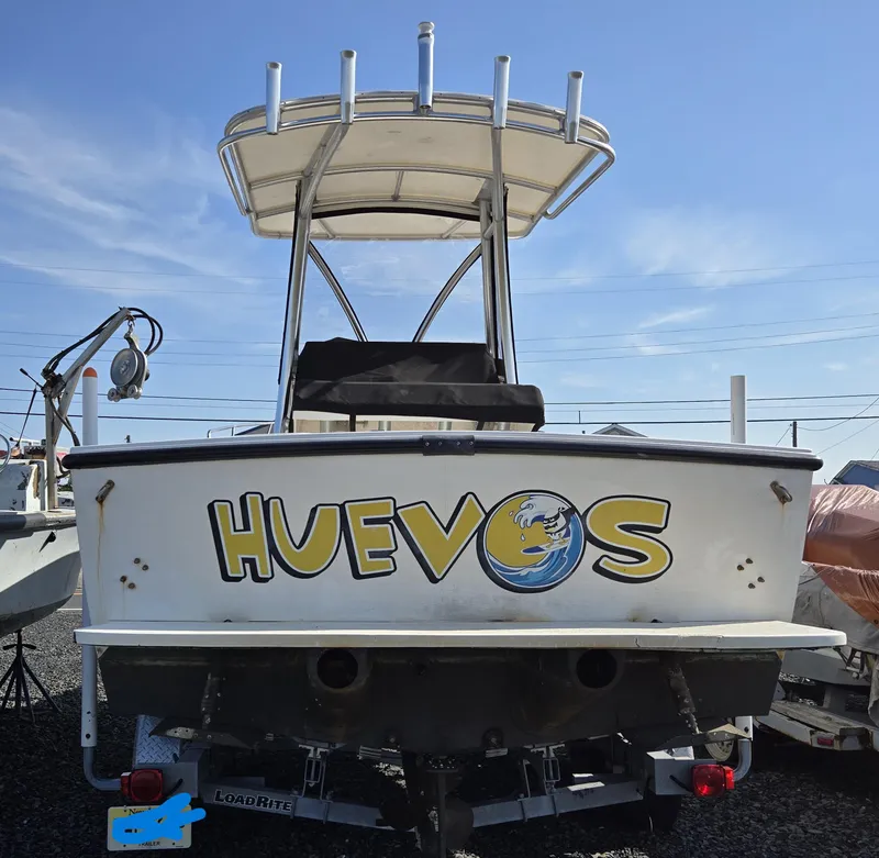 Slide: The Image of 1999 Shamrock 220 Open boat with "HUEVOS" name on the stern, parked outdoors. - 12