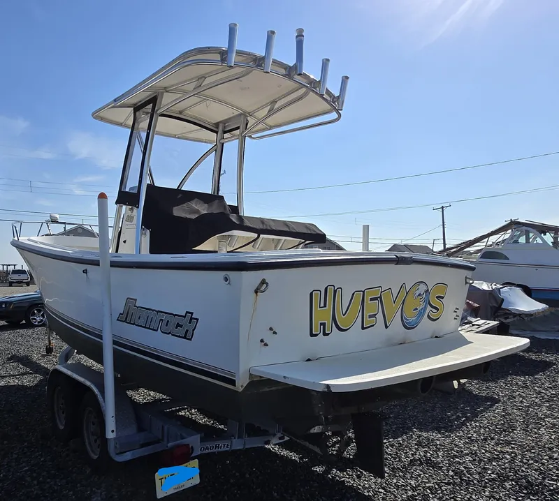 Slide: The Image of 1999 Shamrock 220 Open boat on trailer, named "Huevos," under clear blue sky. - 2