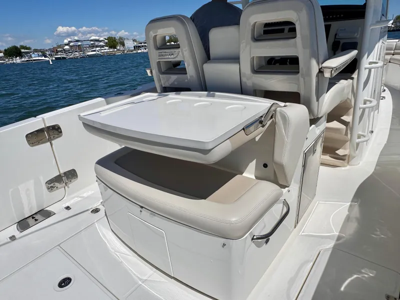 Slide: The Image of 2018 Boston Whaler 330 Outrage boat interior with seating and table, docked by the water. - 8